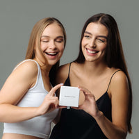 Thumbnail for Two women joyfully holding a gift box from Brother & Sisters, highlighting the Lovers Name Necklace.