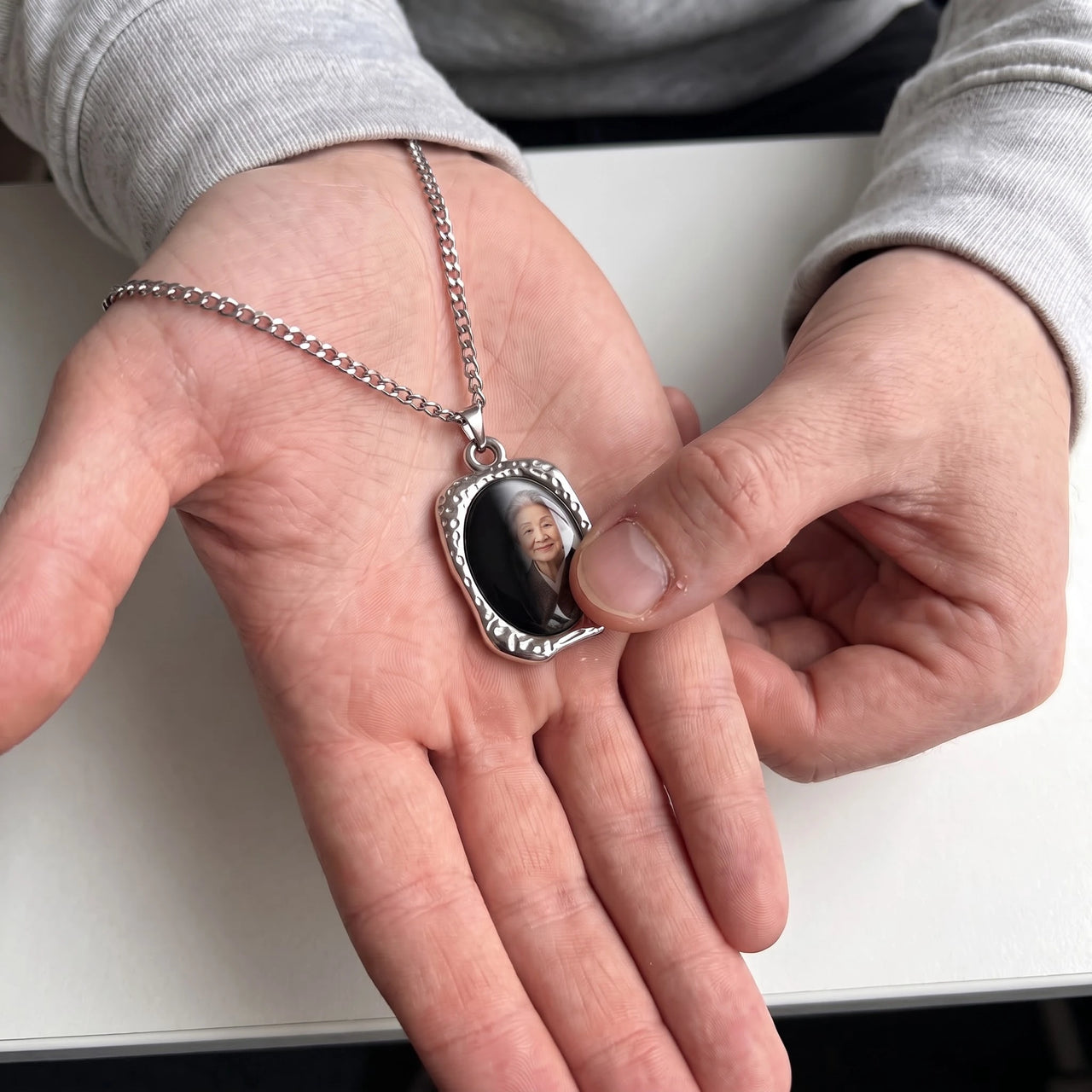 Thumb warming the silver oval pendant: the hidden photo appears under the thumb while the rest stays black | SKU: TPH-OVLN-SILVER