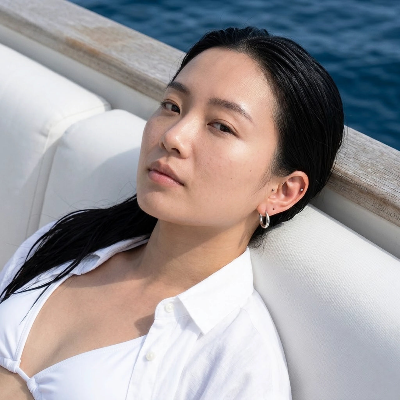 Tiny Huggie Hoops in Silver, worn on a yacht | SKU: 41002-silver